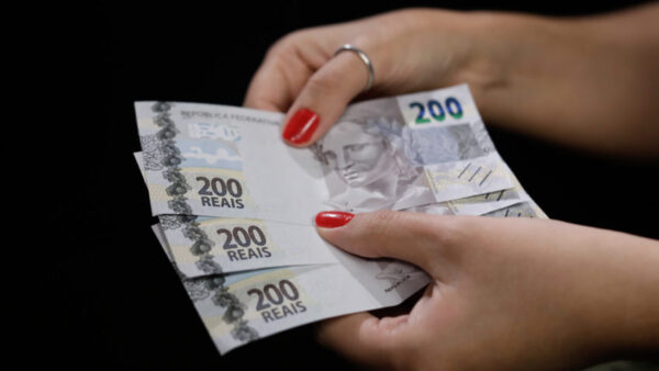 mãos seguram 3 cédulas de R$ 200